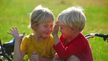 İki küçük çocuklar cycler cihazları yavaş çekim bir çim oturmak ve birbirlerine beşlik. Başarı kavramı. Dostluk kavramı.