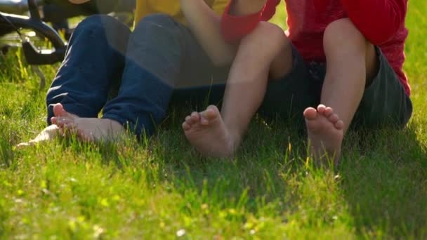 İki küçük çocuklar cycler cihazları yavaş çekim bir çim oturmak ve bir plastik şişe su içmek. Tatlı su kavramı. Dostluk kavramı. — Stok video