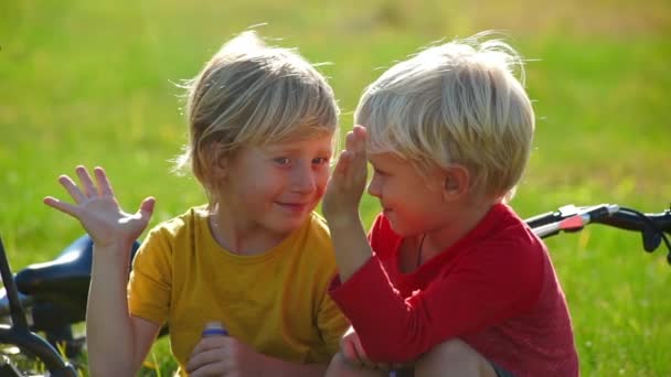 Zeitlupenaufnahme von zwei kleinen Jungen Radler sitzen auf einer Wiese und geben einander fünf. Erfolgskonzept. Freundschaftskonzept. — Stockvideo