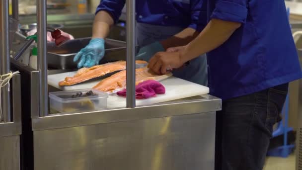 Steadicam tiro do chef em um restaurante japonês com uma cozinha aberta, açougue, preparando um filé de um grande salmão — Vídeo de Stock