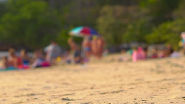 Tiro borrado de uma praia movimentada em trópicos com silhuetas de pessoas passando — Vídeo de Stock