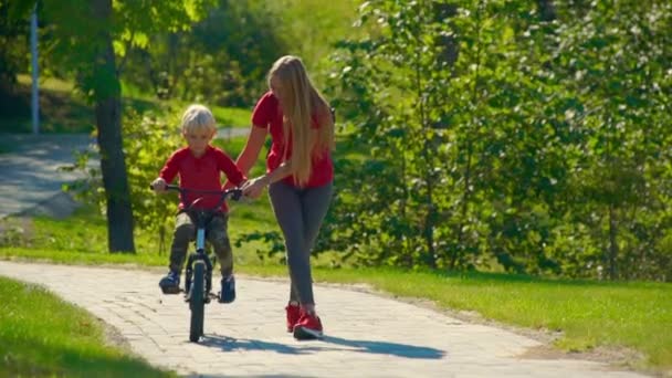 Zeitlupenaufnahme einer jungen Frau, die ihrem kleinen Sohn beibringt, wie man Fahrrad fährt — Stockvideo