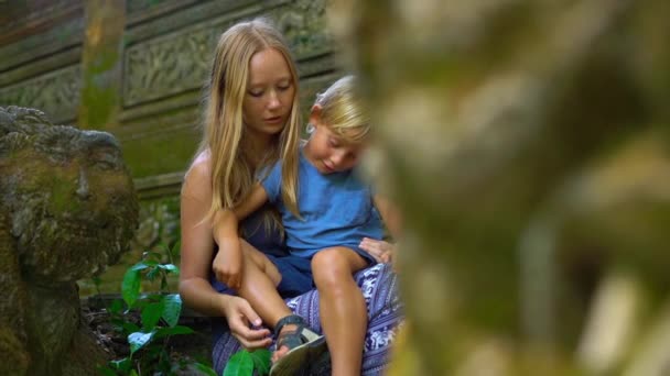 Strzał slowmotion młodą kobietę i jej synek siedząc na schodach w parku ekologicznego małp w Ubud, Indonezja — Wideo stockowe