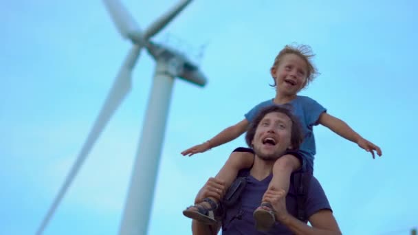 Πατέρας και γιος έχουν διασκέδαση στέκεται κάτω από την ηλεκτρική γεννήτρια άνεμος στην κορυφή του λόφου δίπλα στη θάλασσα. Έννοια της καθαρής ενέργειας. ανανεώσιμη πηγή ενέργειας — Αρχείο Βίντεο