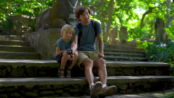 Fotografía en cámara lenta de un joven y su pequeño hijo sentados en las escaleras en el eco-parque forestal Monkeys en Ubud, Indonesia — Vídeo de stock