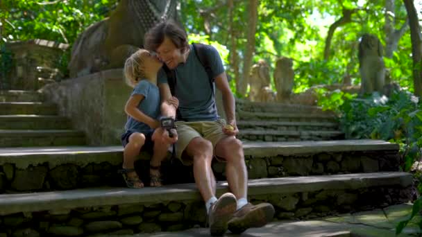 Fotografía en cámara lenta de un joven y su pequeño hijo sentados en las escaleras en el eco-parque forestal Monkeys en Ubud, Indonesia — Vídeo de stock