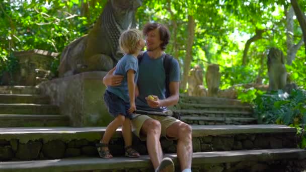 Slow motion shot of a young man and his little son sitting on the stairs in the Monkeys forest eco-park in Ubud, Indonesia — Stock Video