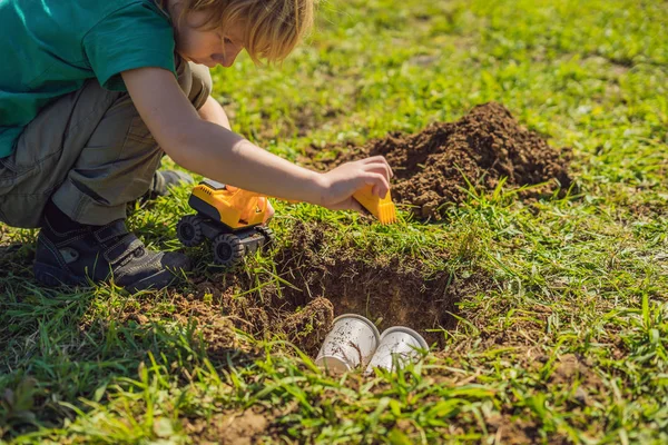 The boy plays recycling. He buries plastic disposable dishes and biodegradable dishes — Stock Photo, Image