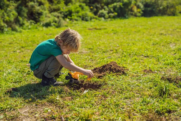 The boy plays recycling. He buries plastic disposable dishes and biodegradable dishes — Stock Photo, Image