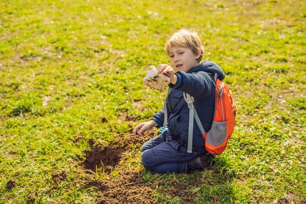 The boy plays recycling. He buries plastic disposable dishes and biodegradable dishes. After a few months, he dug up the dishes and saw that the biodegradable dishes began to decompose and plastic did