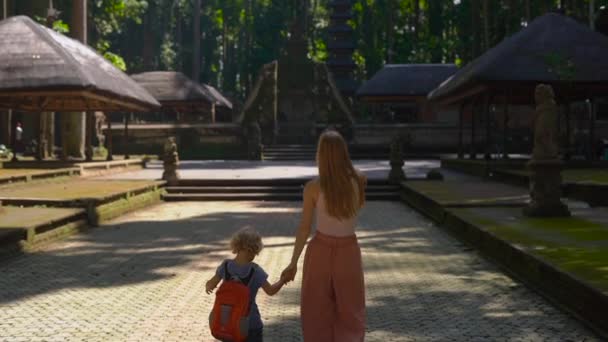 Toma en cámara lenta de una joven mujer y su hijo caminando dentro del bosque de monos Sangeh, en la isla de Bali, Indonesia . — Vídeos de Stock