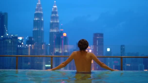 Медленный снимок молодого человека, веселящегося в бассейне на крыше с видом на небоскребы — стоковое видео