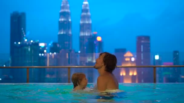 高層ビルを望む屋上プールで楽しんでの幼い息子を持つ若者のスローモーション撮影 — ストック動画