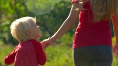 Genç bir kadın ve küçük oğlu birlikte elele bir çimenlikte çalıştıran Slowmotion atış