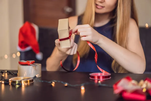 年轻妇女包装礼物在工艺纸与红色和金色丝带为圣诞节 — 图库照片