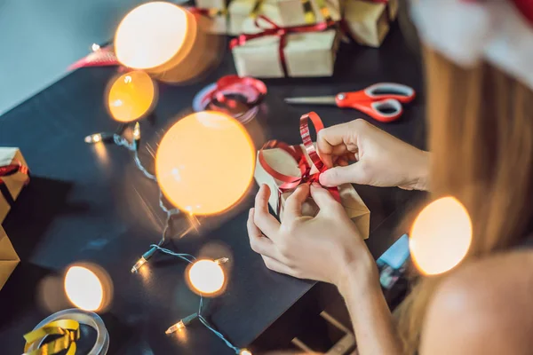 Close-up view of woman packing present in craft paper and festive ribbon for Christmas.