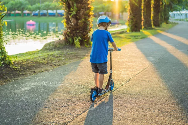 Um menino de capacete montando uma scooter no parque — Fotografia de Stock
