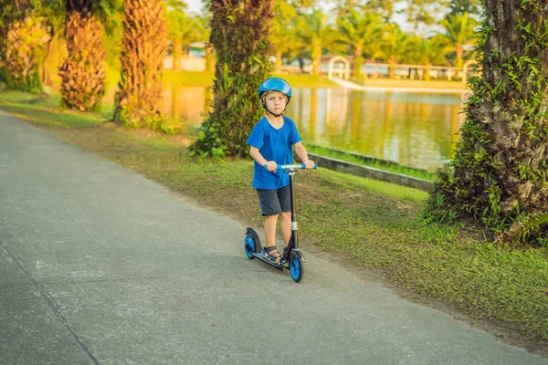 Um menino de capacete montando uma scooter no parque — Fotografia de Stock