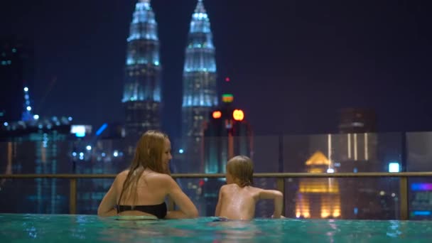 Μια όμορφη νεαρή γυναίκα και τον μικρό γιο να διασκεδάσουν στην πισίνα νερού στον τελευταίο όροφο με θέα σε ουρανοξύστες. Ταξίδια Ασία έννοια — Αρχείο Βίντεο
