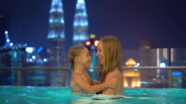 Красивая молодая женщина и ее маленький сын весело провести время в бассейне на крыше с видом на небоскребы. Концепция путешествия в Азию — стоковое видео