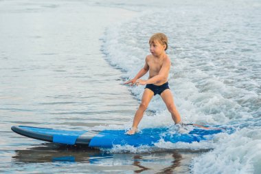 Küçük çocuk acemi kurulu tropik sahilde sörf.