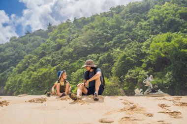 Baba ve oğul Melasti Beach, Bali Adası, Endonezya kumsalda oturuyor. 