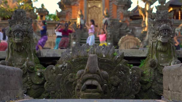 Saraswati-Tempel im Ubud-Dorf auf der Bali-Insel, Indonesien. Steinstatuen im Tempel mit einer verschwommenen Lehrerin, die einer Mädchengruppe einen traditionellen balinesischen Tanz beibringt. — Stockvideo