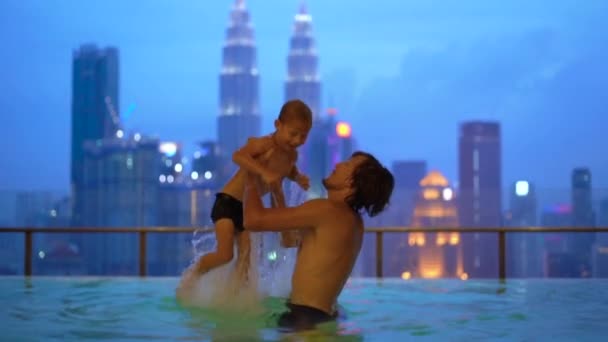 Superzeitlupenaufnahmen eines jungen Mannes und seines kleinen Sohnes amüsieren sich im Wasserbecken auf dem Dach mit Blick auf Wolkenkratzer. Reise nach Asien — Stockvideo