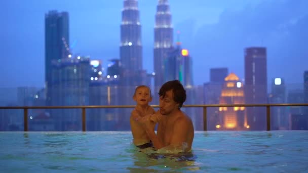 Superslowmotion schot van een jonge man en zijn zoontje veel plezier in water zwembad met uitzicht op de wolkenkrabbers. Reizen naar Asia concept — Stockvideo