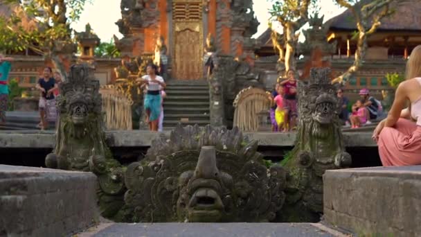 Slowmotion sköt. Saraswati templet i Ubud village på ön Bali, Indonesien. Sten statyer inne i templet med suddig en kvinna lärare som undervisar grupp flickor en traditionell — Stockvideo