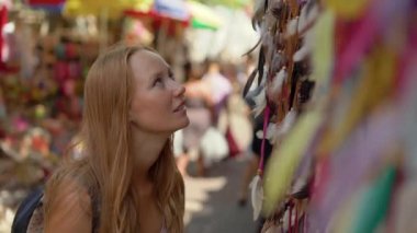 Bir genç kadın seyahat Hediyelik eşya seçme bir Asya pazarı ziyaret kadeh Slowmotion