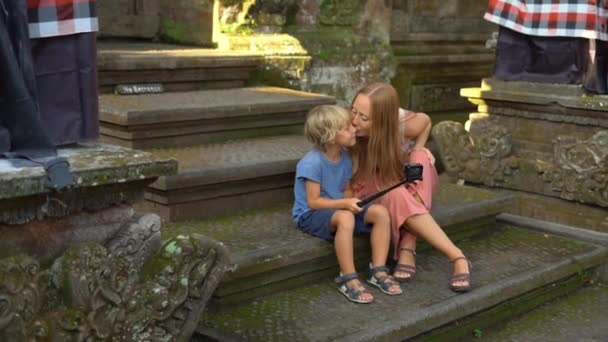 Zeitlupenaufnahmen einer schönen jungen Frau und ihres kleinen Sohnes machen ein Selfie mit einer Actionkamera auf der Treppe des balinesischen Tempels. Reise nach Indonesien. Reisen mit Kindern — Stockvideo