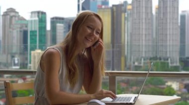 Genç kadın serbest meslek amele üstünde onu laptop gökdelenler tam bir şehir merkezinin bir arka plan ile bir balkon. O telefon aramayý cevaplar