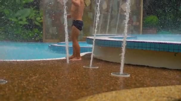 Slowmotion tiro de um menino em um parque tropical brincando com fontes — Vídeo de Stock