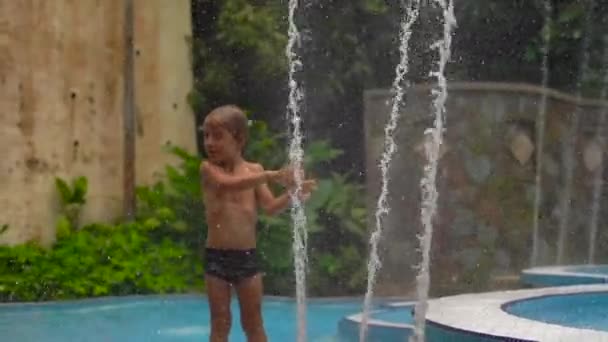 Plan au ralenti d'un petit garçon dans un parc tropical jouant avec des fontaines — Video