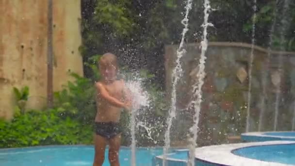 Slowmotion skott av en liten pojke i en tropisk park som leker med fontäner — Stockvideo