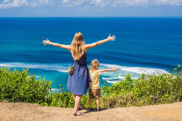 Happy mother and son on cliff above empty paradise beach of Nyang Nyang with blue sea in Bali island, Indonesia.