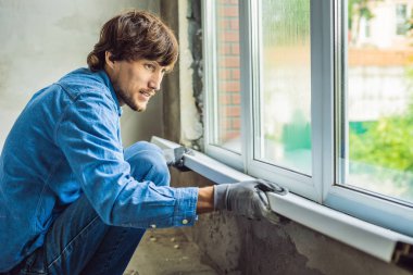Evde pencere yüklemesi mavi tişörtlü adam.