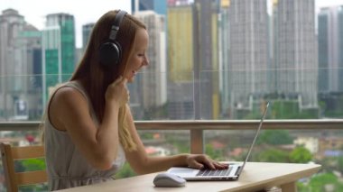 Genç kadın serbest meslek amele üstünde onu laptop gökdelenler tam bir şehir merkezinin bir arka plan ile bir balkon. Internet üzerinden bir öğrenciyle bir görüşme, uzak techer vardır