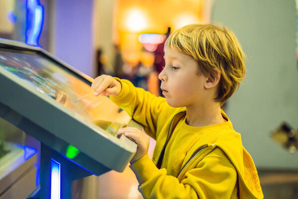 The boy in the yellow jacket uses a touch screen