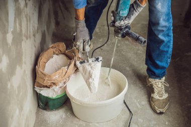 Close-up of male painter kneading putty in bucket with hand-held mixer. clipart