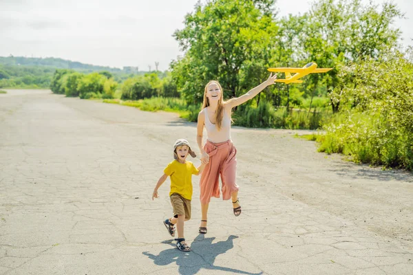 Mãe e filho felizes brincando com avião de brinquedo contra o fundo da pista antiga. Viajar com conceito de crianças — Fotografia de Stock