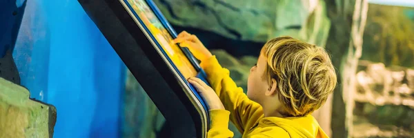 De jongen in de gele jas maakt gebruik van een touchscreen Banner, lange notatie — Stockfoto