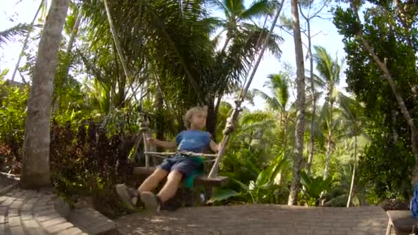 熱帯のジャングルでスイングの小さな男の子を押す認識できない女性のスローモーション — ストック動画