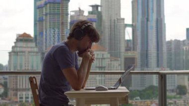 Balkon şehir merkezinin arka plan ile dizüstü bilgisayarda çalışırken düşünme genç erkek serbest meslek.