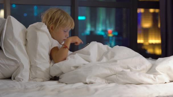 Маленький Блондинка Сидить Ліжку Вночі Грає Цифровий Планшет Силуетами Міста — стокове відео