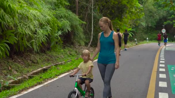 Steadicam schot van een jonge vrouw en haar zoontje op een run bike uitgevoerd in een park. Sport met kinderen concept — Stockvideo