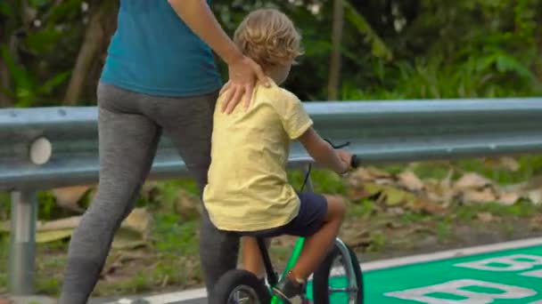 Steadicam πλάνο του μια νεαρή γυναίκα και το μικρό γιο της σε ένα ποδήλατο τρέχει σε ένα πάρκο. Αθλητικά με παιδιά έννοια — Αρχείο Βίντεο