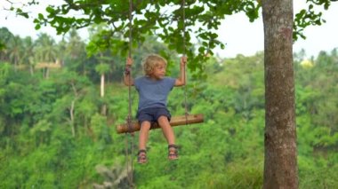 Küçük Çocuk salıncaklar tropikal bir parkta üzerinde sallanan yavaş hareket atış. 