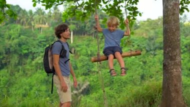 Genç adam küçük oğlu tropikal parkta salıncak iterek yavaş çekim. 